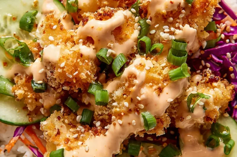 Vibrant close-up vertical shot of bang bang chicken bowl overflowing with crispy sauced chicken, purple cabbage, carrots, and sesame seeds