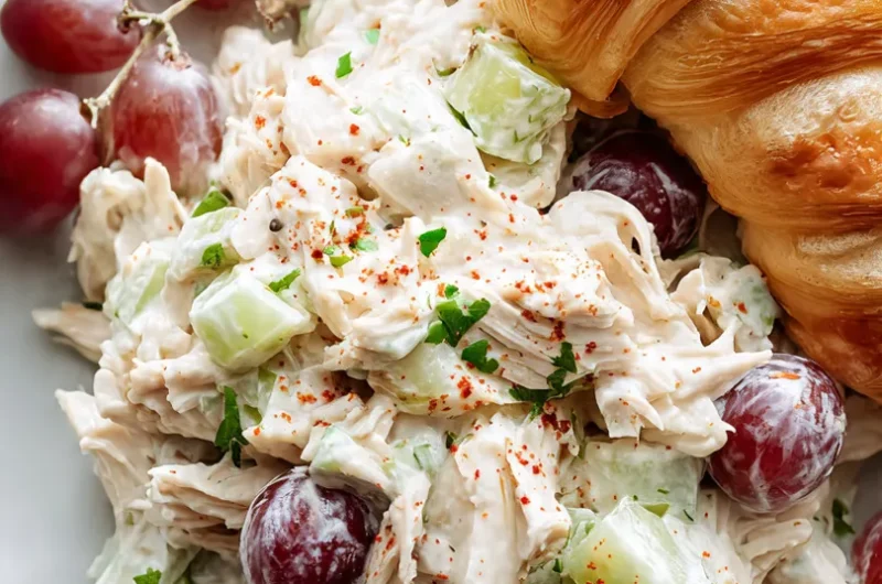 Extreme close-up vertical shot of creamy protein chicken salad showing shredded chicken, red grapes, celery, and smoked paprika.