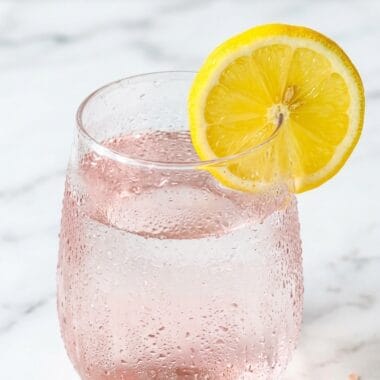 Glass of pink salt fasting drink with lemon and Himalayan salt crystals on white marble