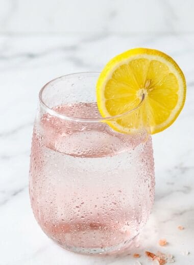 Glass of pink salt fasting drink with lemon and Himalayan salt crystals on white marble