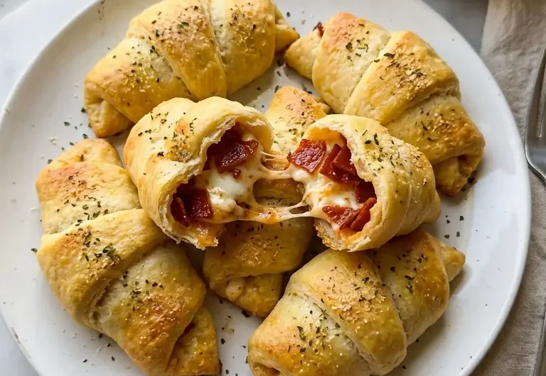 Golden pepperoni cream cheese crescent rolls on a white ceramic plate with marinara dipping sauce