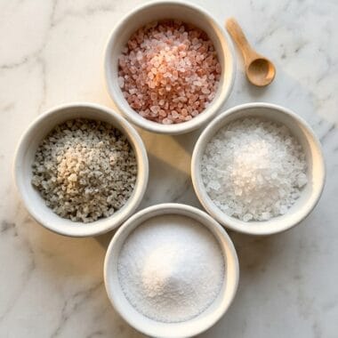 Four types of salt in white bowls showing pink salt vs sea salt vs table salt comparison