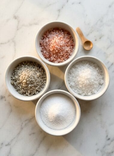 Four types of salt in white bowls showing pink salt vs sea salt vs table salt comparison