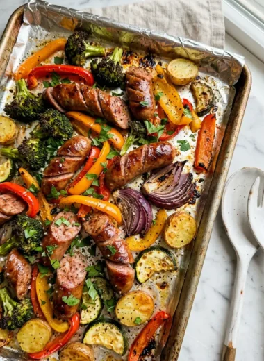 Sheet pan sausage and veggies with roasted bell peppers, broccoli, and baby potatoes on a foil-lined baking sheet