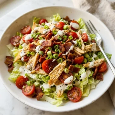 BLT chicken salad in a white ceramic bowl with crispy bacon, tomatoes, and creamy dressing on white marble