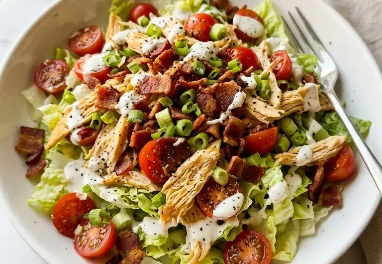 BLT chicken salad in a white ceramic bowl with crispy bacon, tomatoes, and creamy dressing on white marble