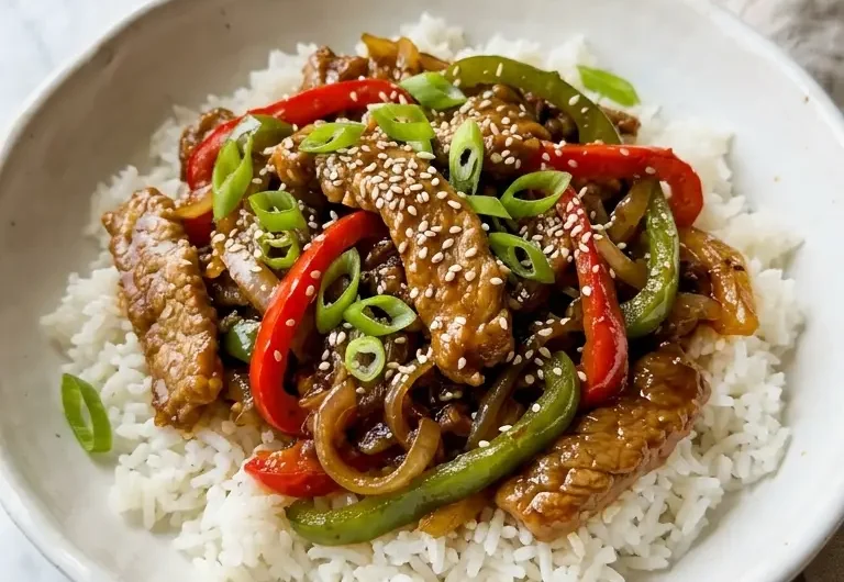 Sizzling Chinese Pepper Steak with onions in a white ceramic bowl over jasmine rice
