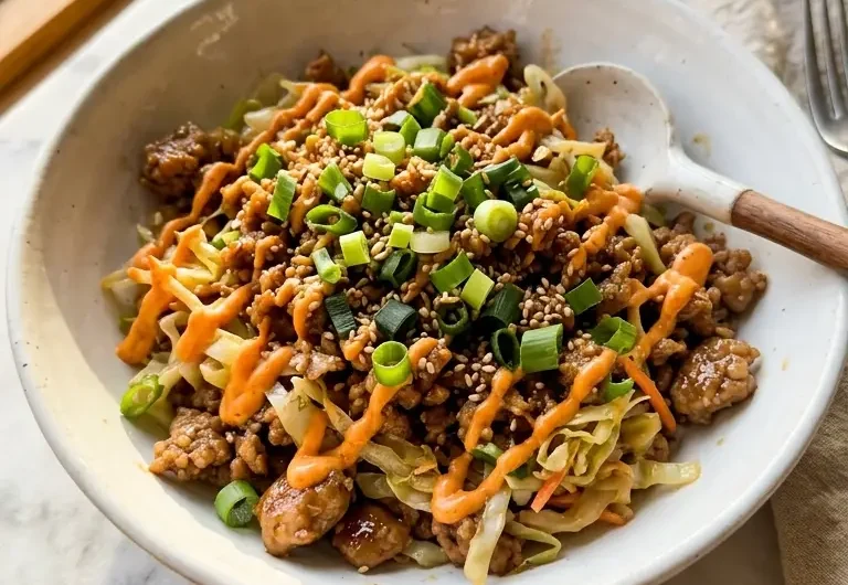 high protein egg roll in a bowl served in a white ceramic bowl topped with green onions and sriracha drizzle