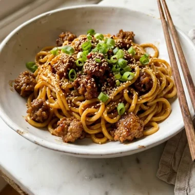 Close-up of sticky beef noodles in a white bowl topped with spring onions and sesame seeds