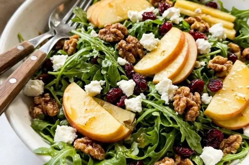 apple arugula salad in a white ceramic bowl with walnuts, goat cheese, and cranberries