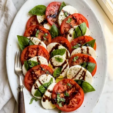 Caprese Salad with Balsamic Glaze on a white platter with fresh basil and glossy glaze