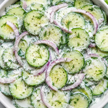 creamy cucumber dill salad in a white ceramic bowl with fresh dill and scallions