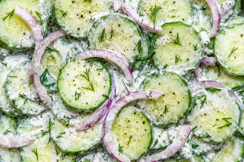creamy cucumber dill salad in a white ceramic bowl with fresh dill and scallions