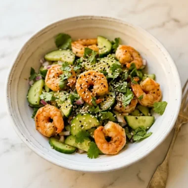 Cucumber shrimp salad in a white ceramic bowl with fresh avocado and lime wedges