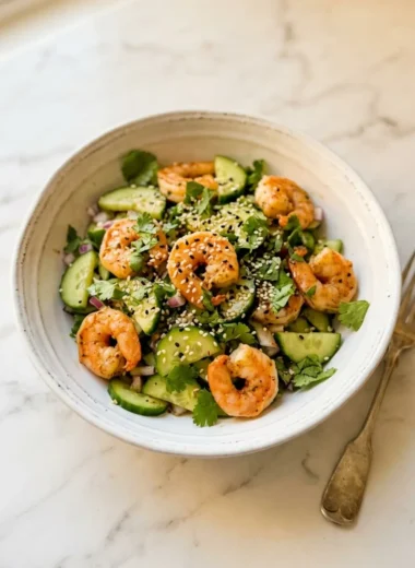 Cucumber shrimp salad in a white ceramic bowl with fresh avocado and lime wedges