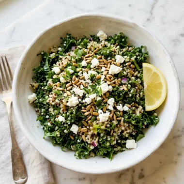 kale quinoa salad with lemon dressing in white bowl with feta and lemon wedge