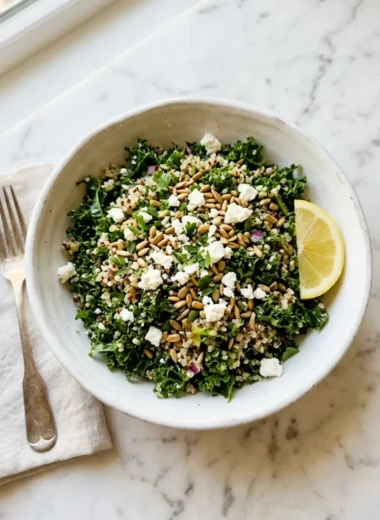 kale quinoa salad with lemon dressing in white bowl with feta and lemon wedge