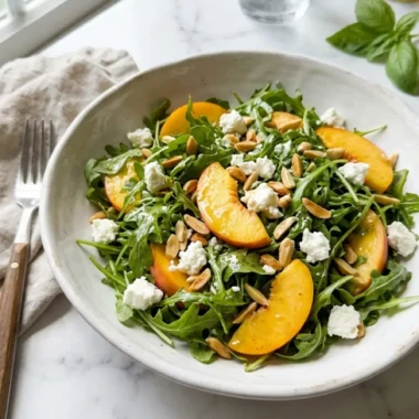 Summer Peach Salad in white bowl with arugula peach slices goat cheese and almonds
