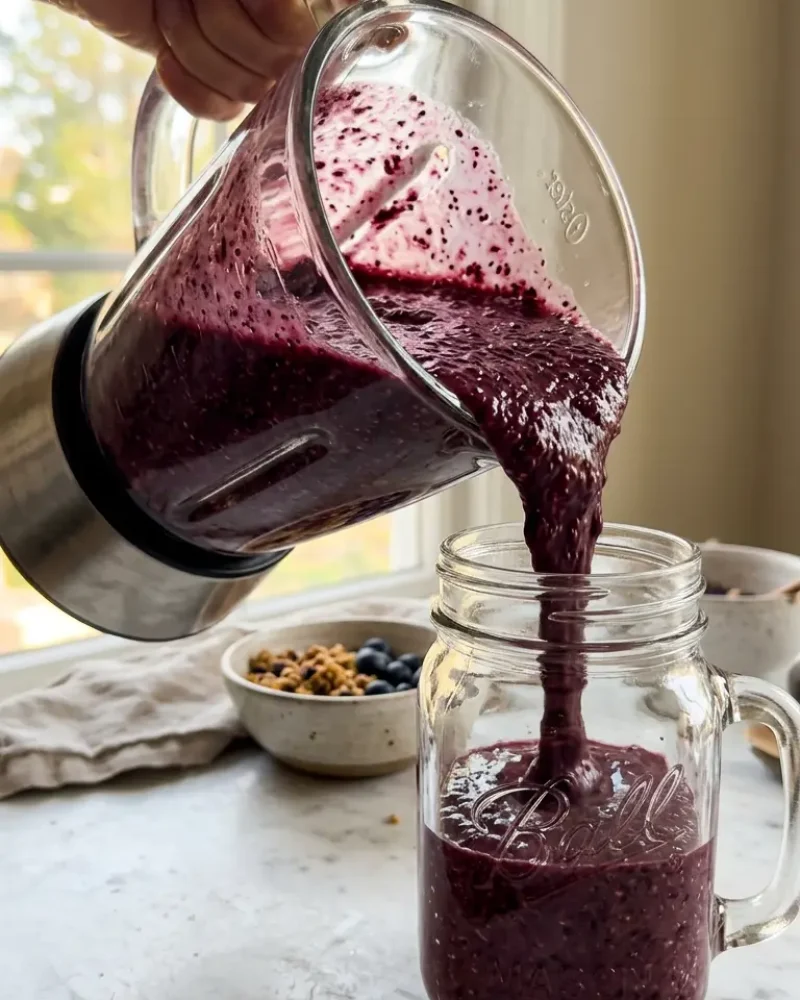 Thick purple chia seed smoothie being poured from blender into mason jar