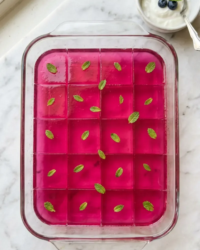 Overhead view of Dr Oz pink gelatin recipe squares in glass dish ready to serve with yogurt