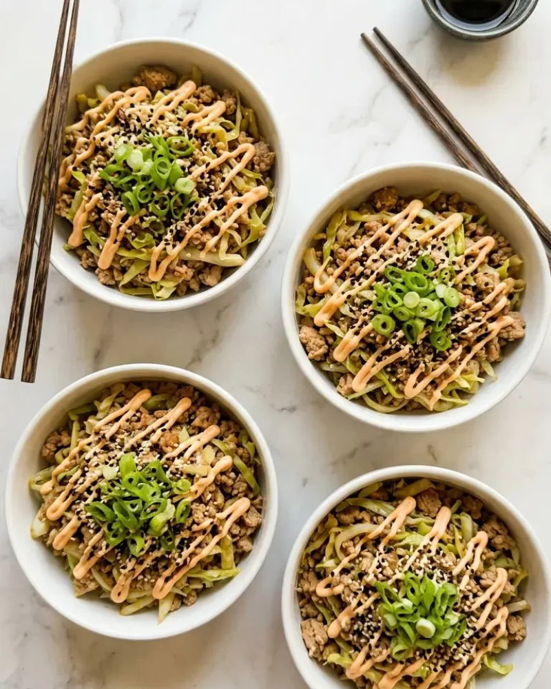 overhead view of four bowls of high protein egg roll in a bowl with green onions and chopsticks on white marble