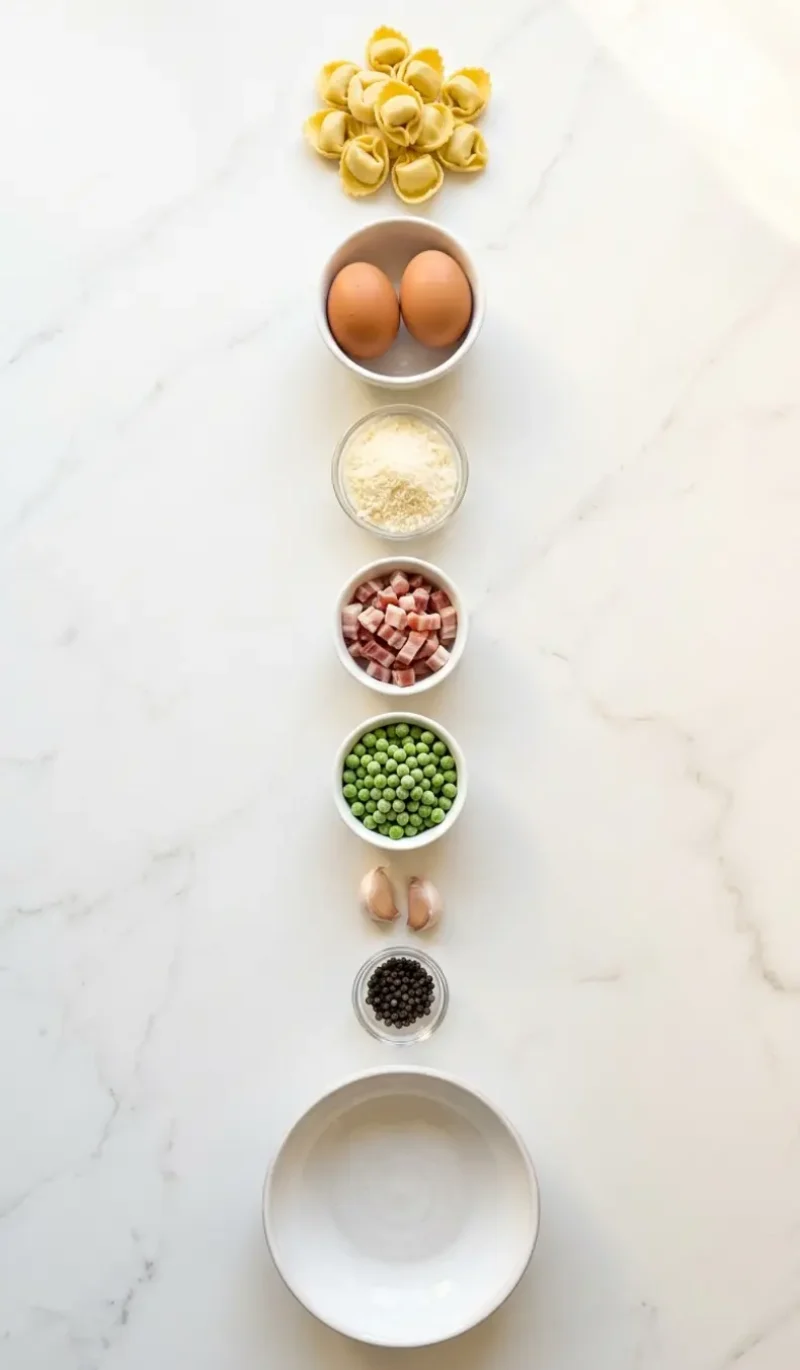 Exploded view of all 7 ingredients for Tortellini Carbonara arranged vertically on white marble